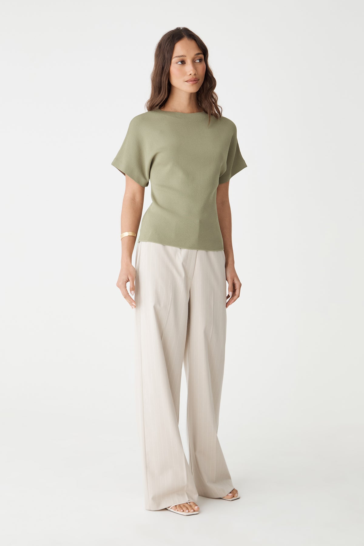 Front view of the soft khaki relaxed knit top, full length with cream trousers