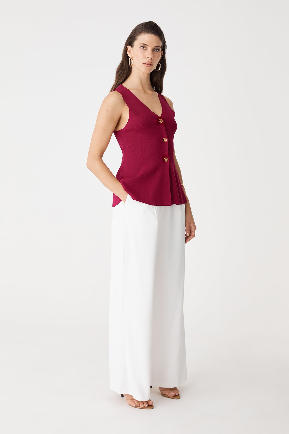 Side view of the fuchsia peplum knit top worn with white wide-leg trousers