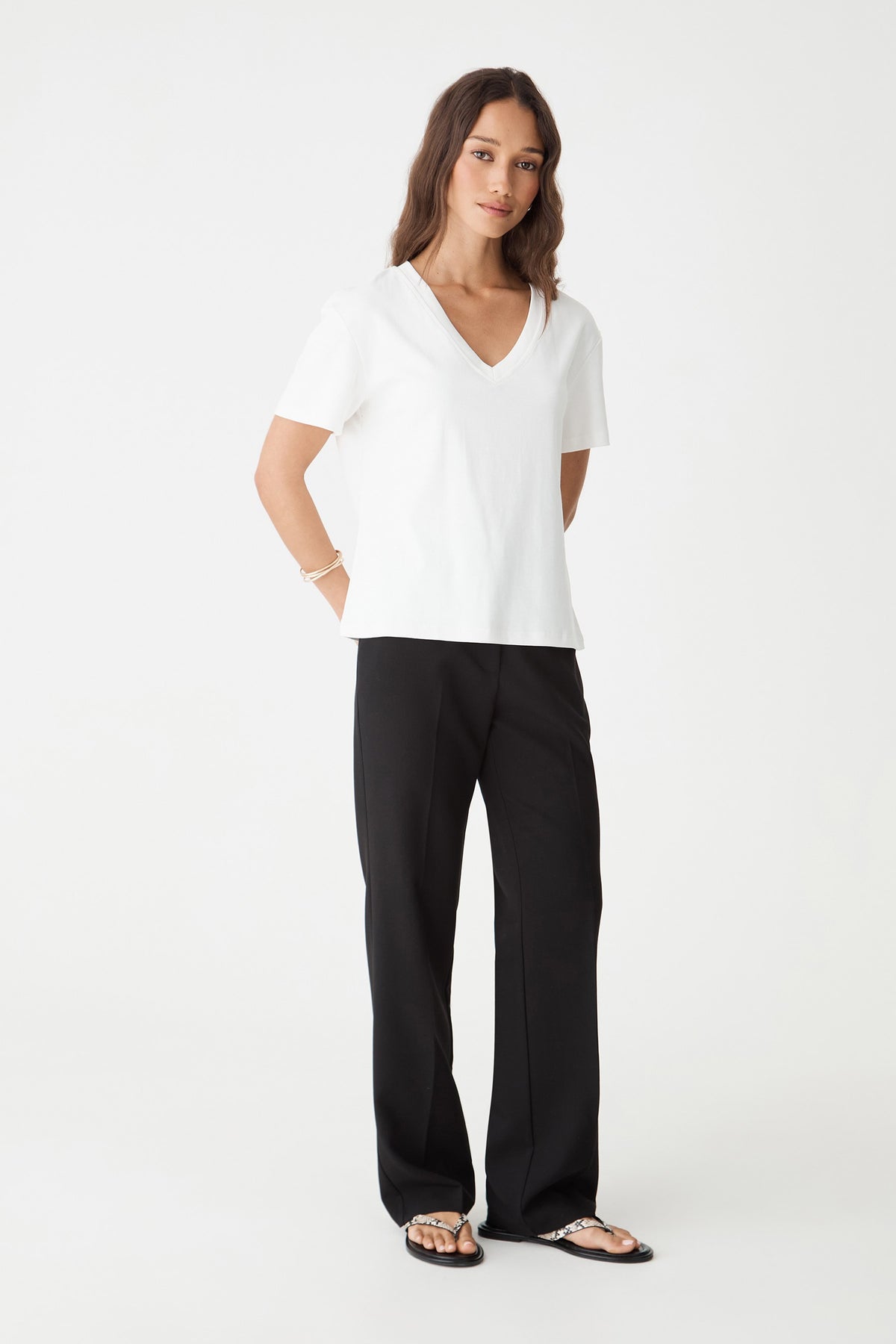Front view of the white May V-Neck Cotton T-Shirt, loose cut untucked over black trousers