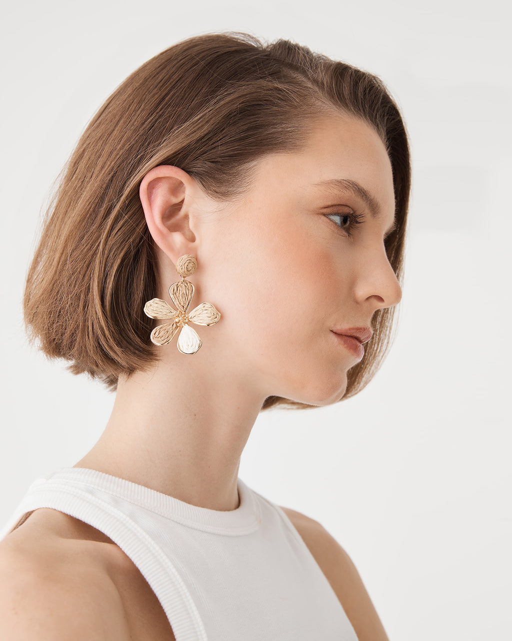 Close-up of beige raffia floral drop earring with beaded centre, worn
